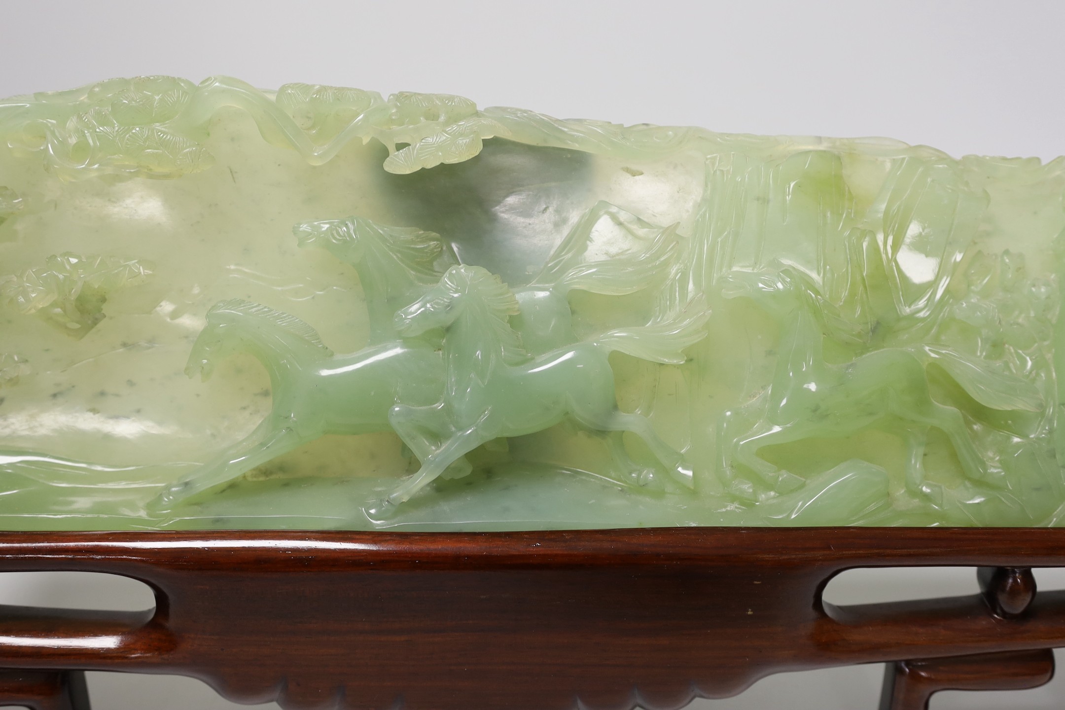 A large Chinese bowenite jade plaque of galloping horses, wood stand, 40cm wide